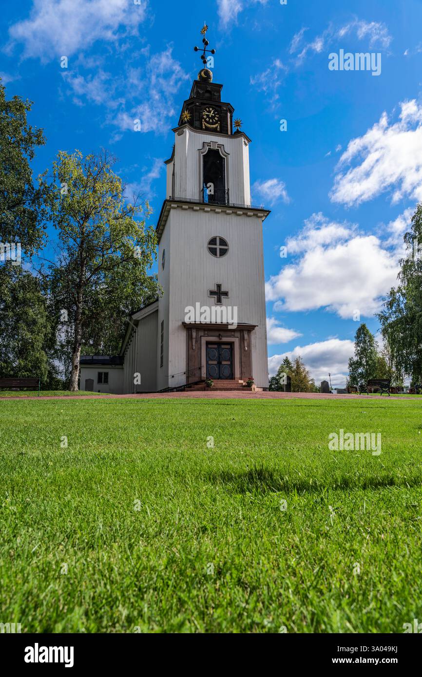 L'erba verde brillante incornicia la Chiesa di Svezia a Idre Dalarna. L'edificio presenta una distinta torre dell'orologio sotto un vibrante cielo blu con nuvole Foto Stock