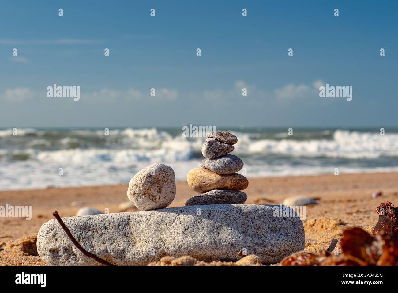 Bellissima installazione di pietre marine sulla spiaggia. Una torre di ciottoli sorge su una grande pietra sullo sfondo dell'oceano. Cielo limpido, giorno di sole Foto Stock