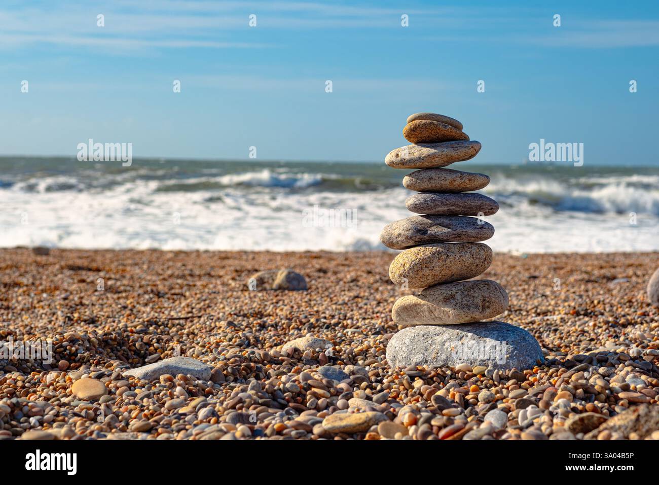 Bellissima installazione di pietre marine sulla spiaggia. Una torre di ciottoli sorge su una grande pietra sullo sfondo dell'oceano. Cielo limpido e grande W Foto Stock