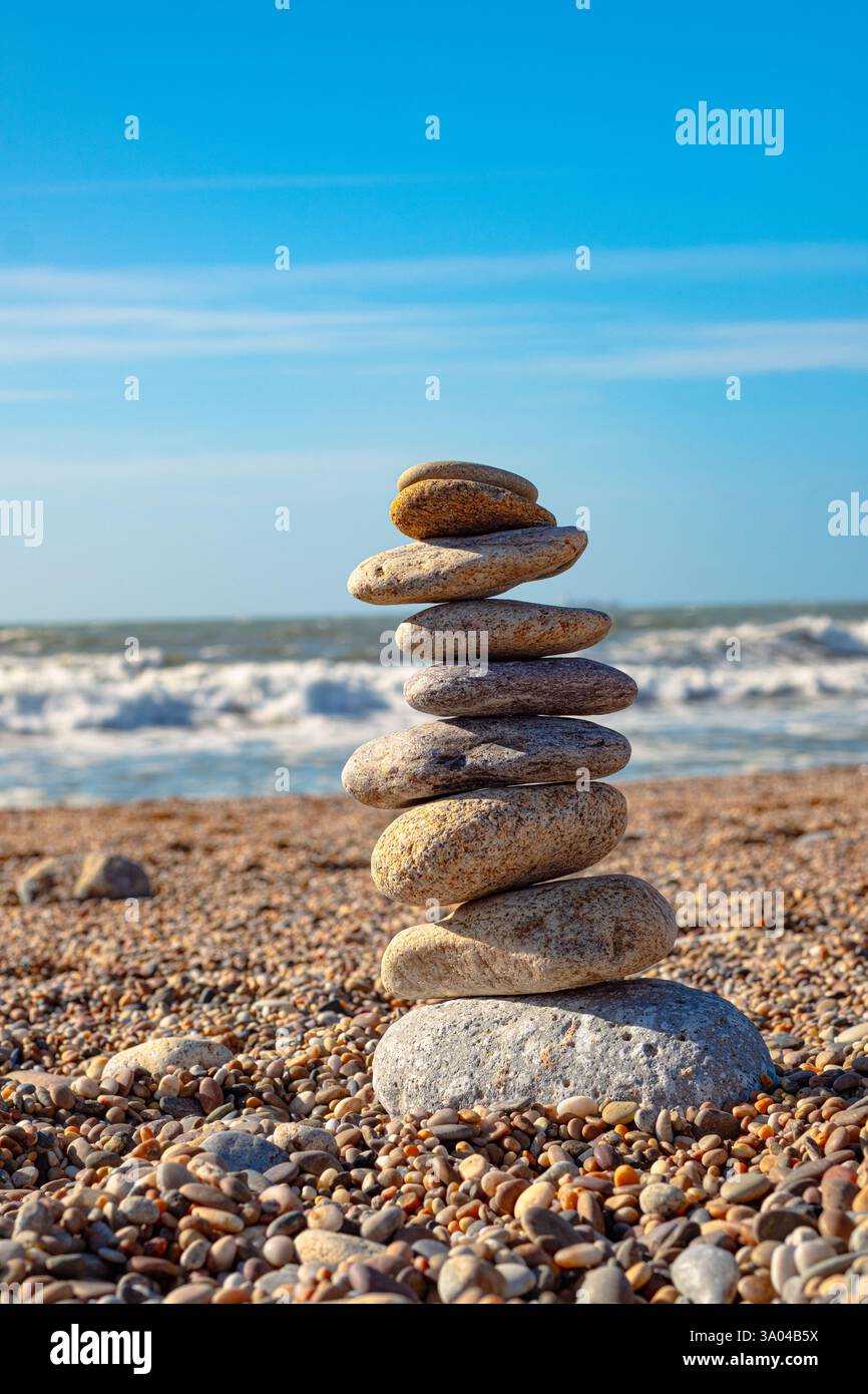 Bellissima installazione di pietre marine sulla spiaggia. Una torre di ciottoli sorge su una spiaggia di sabbia sullo sfondo dell'oceano. Cielo limpido e grande wa Foto Stock
