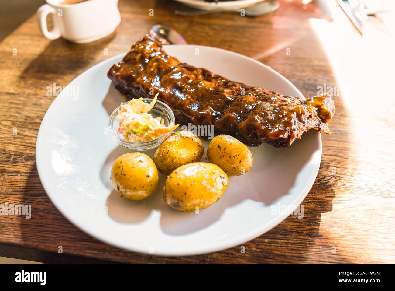 Succulente costolette di maiale con salsa barbecue, patate e cavolo su piatto bianco alla luce del giorno al ristorante Foto Stock