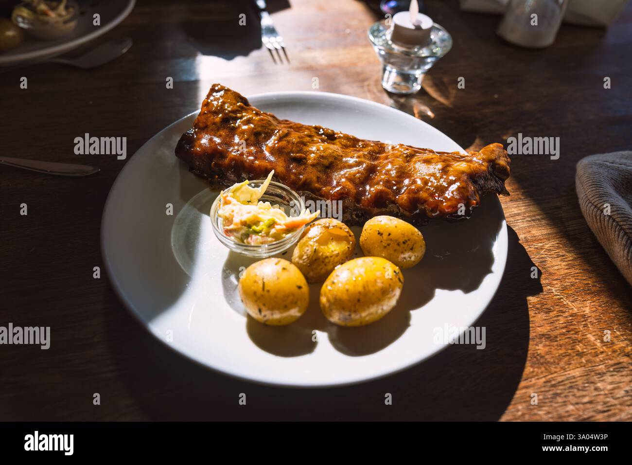 Succulente costolette di maiale con salsa barbecue, patate e cavolo su piatto bianco alla luce del giorno al ristorante Foto Stock