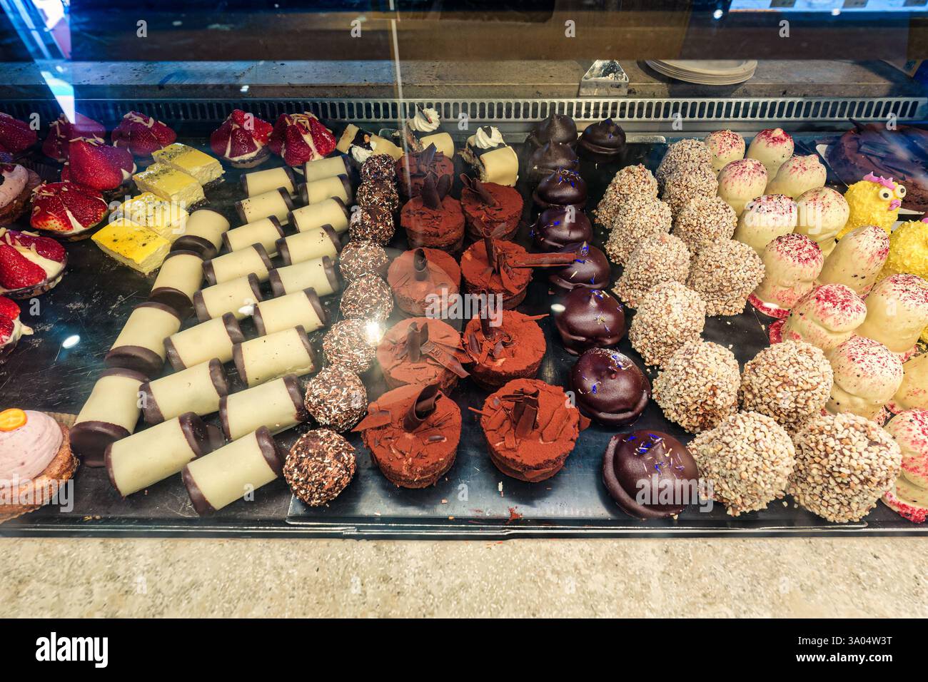 Splendida gamma di dessert gourmet assortiti in vetrina di panifici, con vari colori, texture e decorazioni Foto Stock