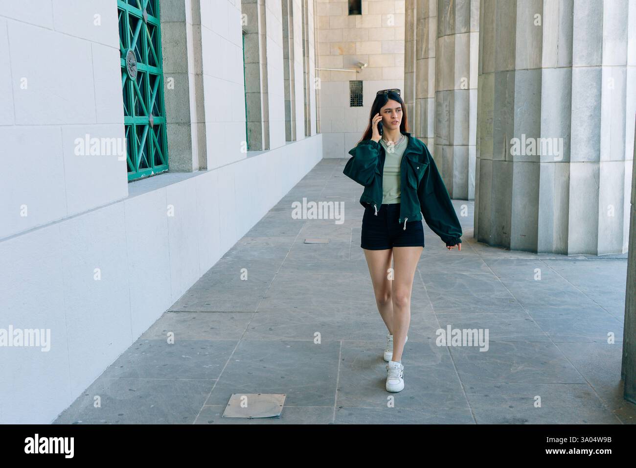 Giovane donna ispanica che cammina in un'elegante galleria della città mentre parla al telefono Foto Stock