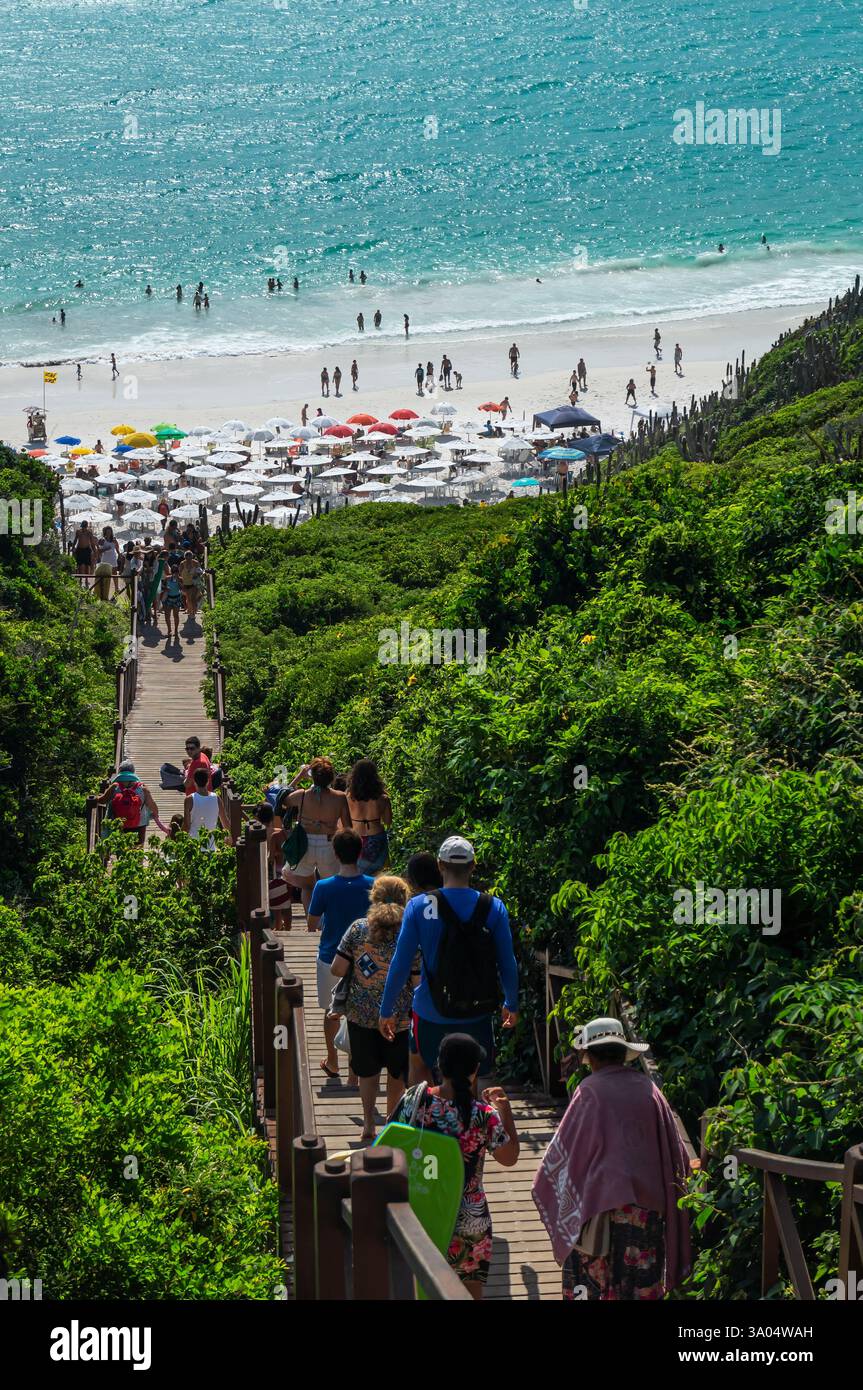 I turisti camminano lungo la scala di legno che conduce alla spiaggia di Pontal do Atalaia, nelle acque azzurre della baia di Guriri, sotto le calde giornate di sole della mattina d'estate. Foto Stock