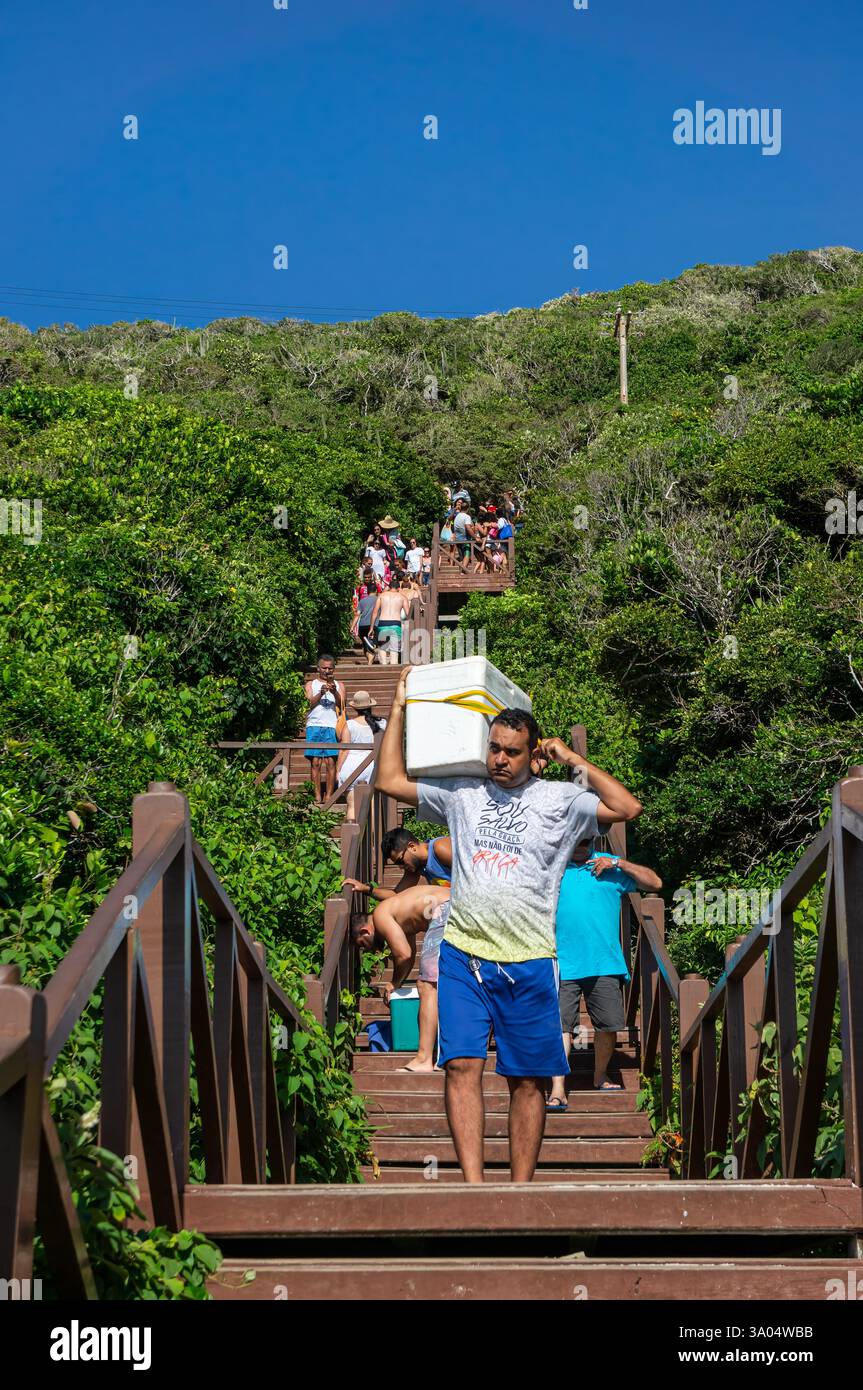 I turisti scendono lungo la lunga scalinata in legno che conduce alla spiaggia di Pontal do Atalaia sotto il cielo azzurro e luminoso della mattina d'estate. Foto Stock