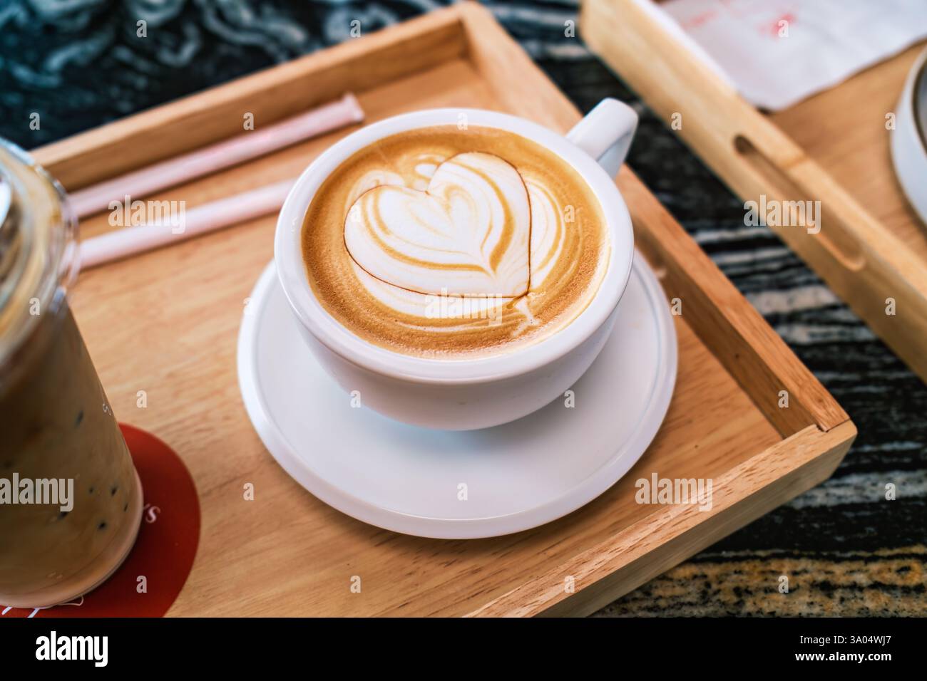Design a forma di cuore con latte art caldo realizzato splendidamente in tazza in ceramica bianca su vassoio in legno nella caffetteria Foto Stock