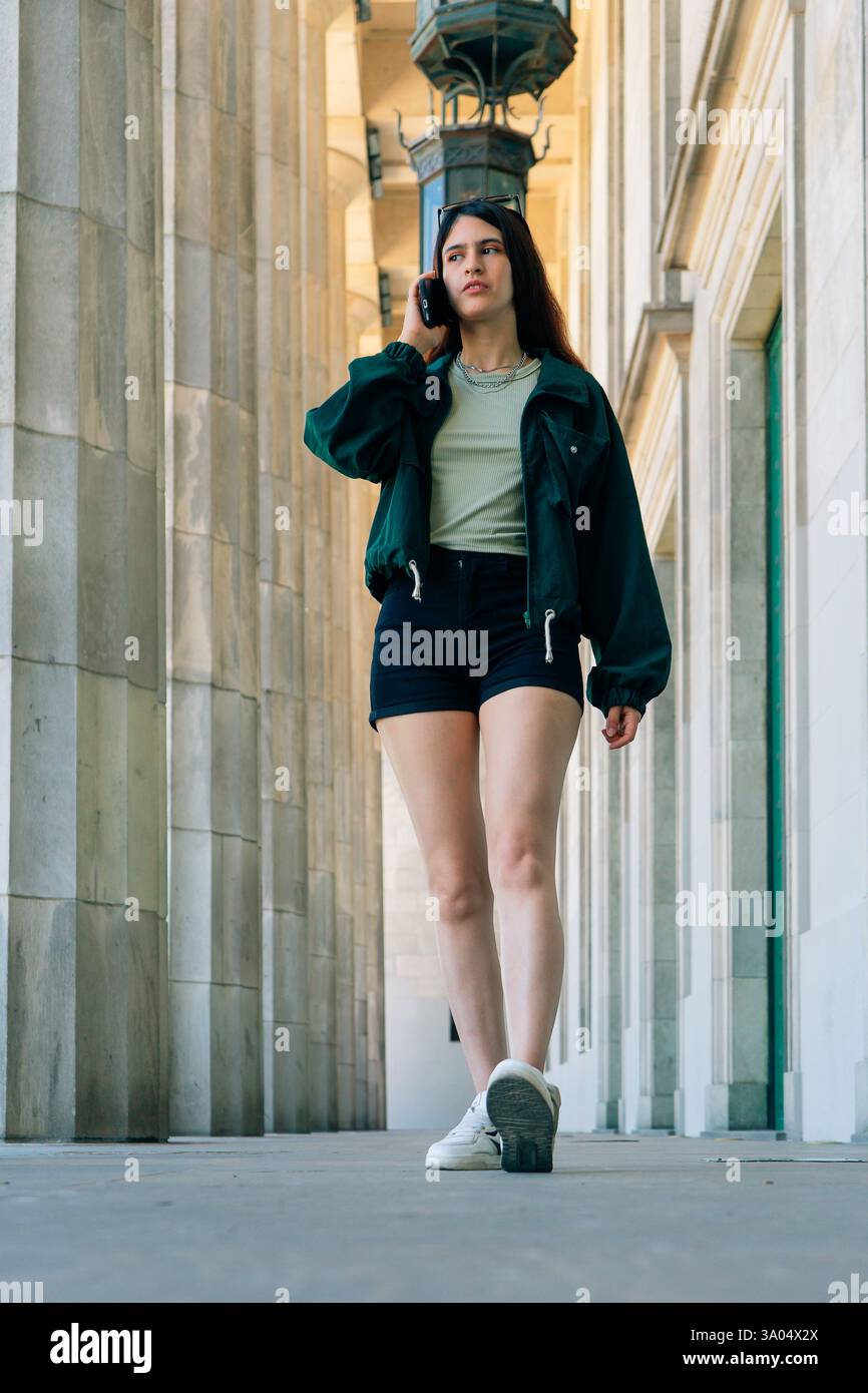 Una giovane donna latina elegante cammina in un corridoio con colonne e parla al telefono Foto Stock