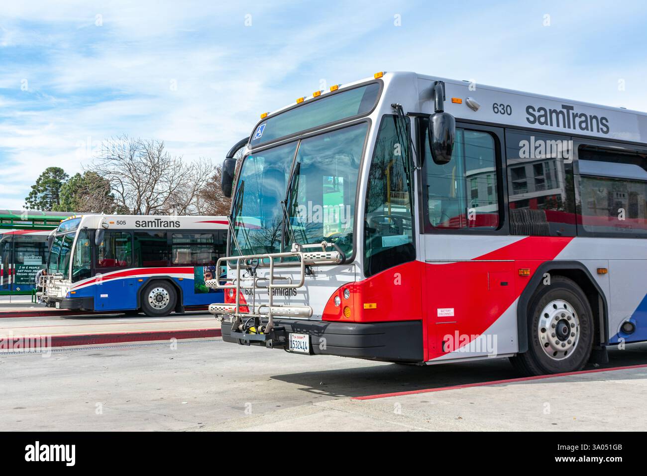 Due autobus Samtrans in livrea rossa, bianca e blu parcheggiati in un centro di transito. Vista laterale anteriore - Redwood City, California, Stati Uniti - 23 febbraio 2025 Foto Stock