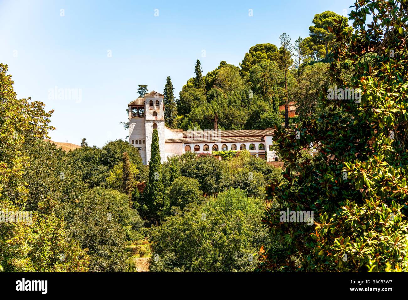 Generalife da lontano nel complesso dell'Alhambra con lussureggiante vegetazione mediterranea che circonda l'architettura moresca sotto il soleggiato cielo spagnolo Foto Stock