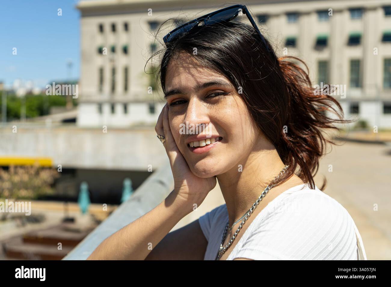 Ritratto di una giovane donna latina sorridente con gli occhiali da sole sulla testa, appoggiata su una ringhiera in un ambiente urbano Foto Stock