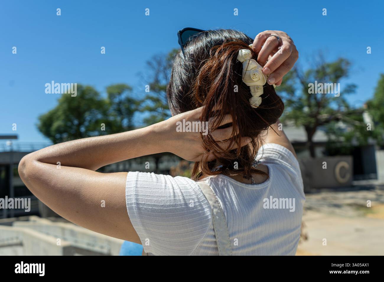 Elegante donna latina che si prepara a decorare i capelli con ornamenti floreali in una giornata di sole, godendosi il clima caldo Foto Stock
