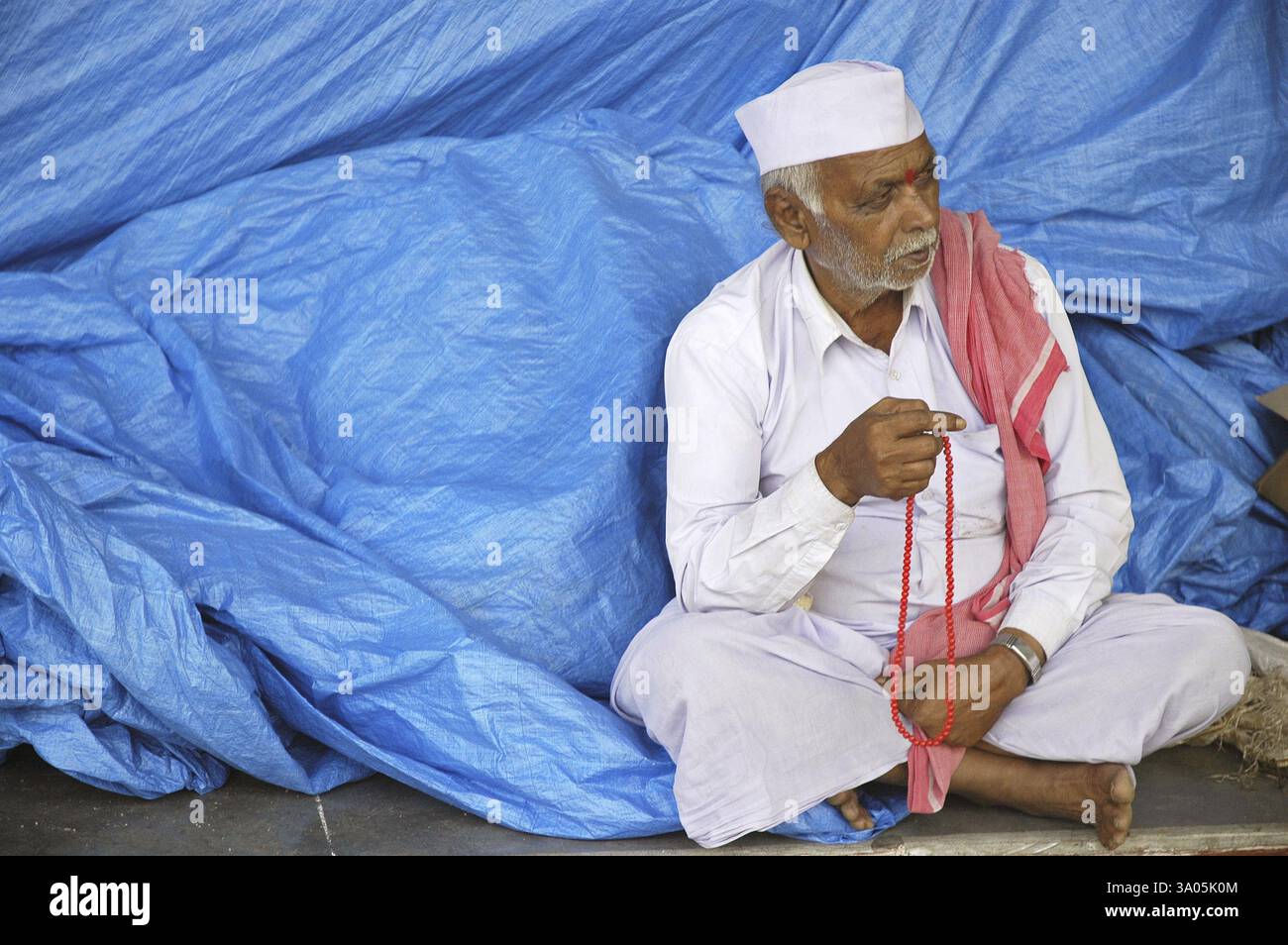 Un pellegrino con rosario rosso in contrasto con lo sfondo blu durante la festa giainista di Mahamastakabhishek, che si tiene una volta ogni 12 anni, Shravanbelgola, Foto Stock