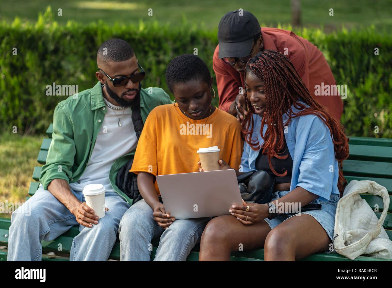 Allegro gruppo di amici afroamericani che bevono caffè e lavorano su computer portatili nel parco verde Foto Stock