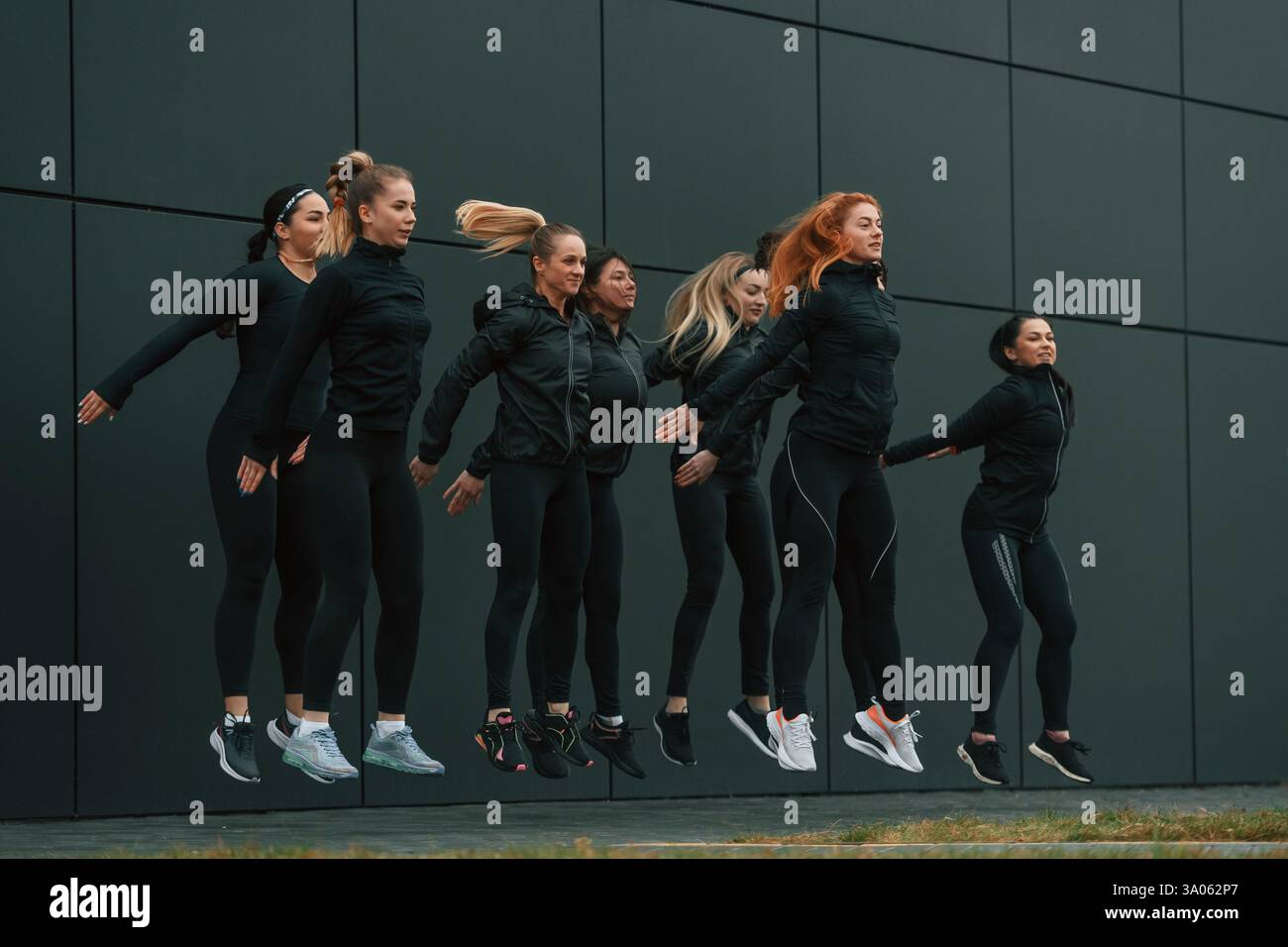 Saltando insieme. Un gruppo di donne sportive si trova all'aperto vicino all'edificio nero. Foto Stock
