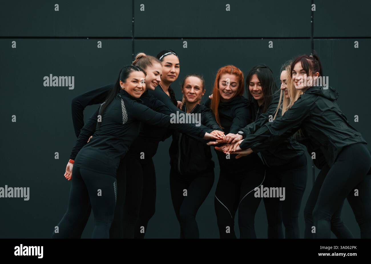 Concezione del lavoro di squadra. Un gruppo di donne sportive si trova all'aperto vicino all'edificio nero. Foto Stock