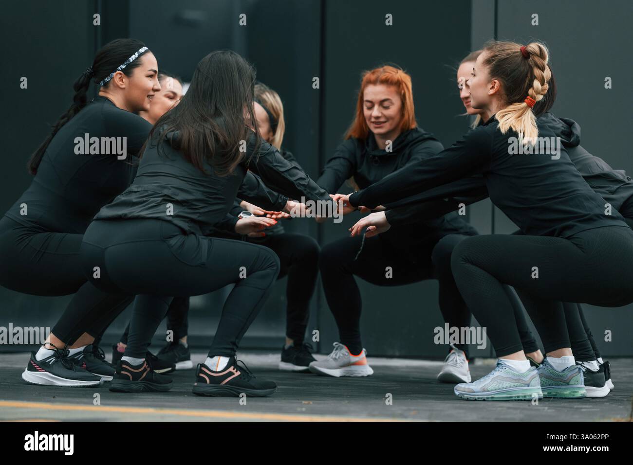 Concezione del lavoro di squadra. Un gruppo di donne sportive si trova all'aperto vicino all'edificio nero. Foto Stock