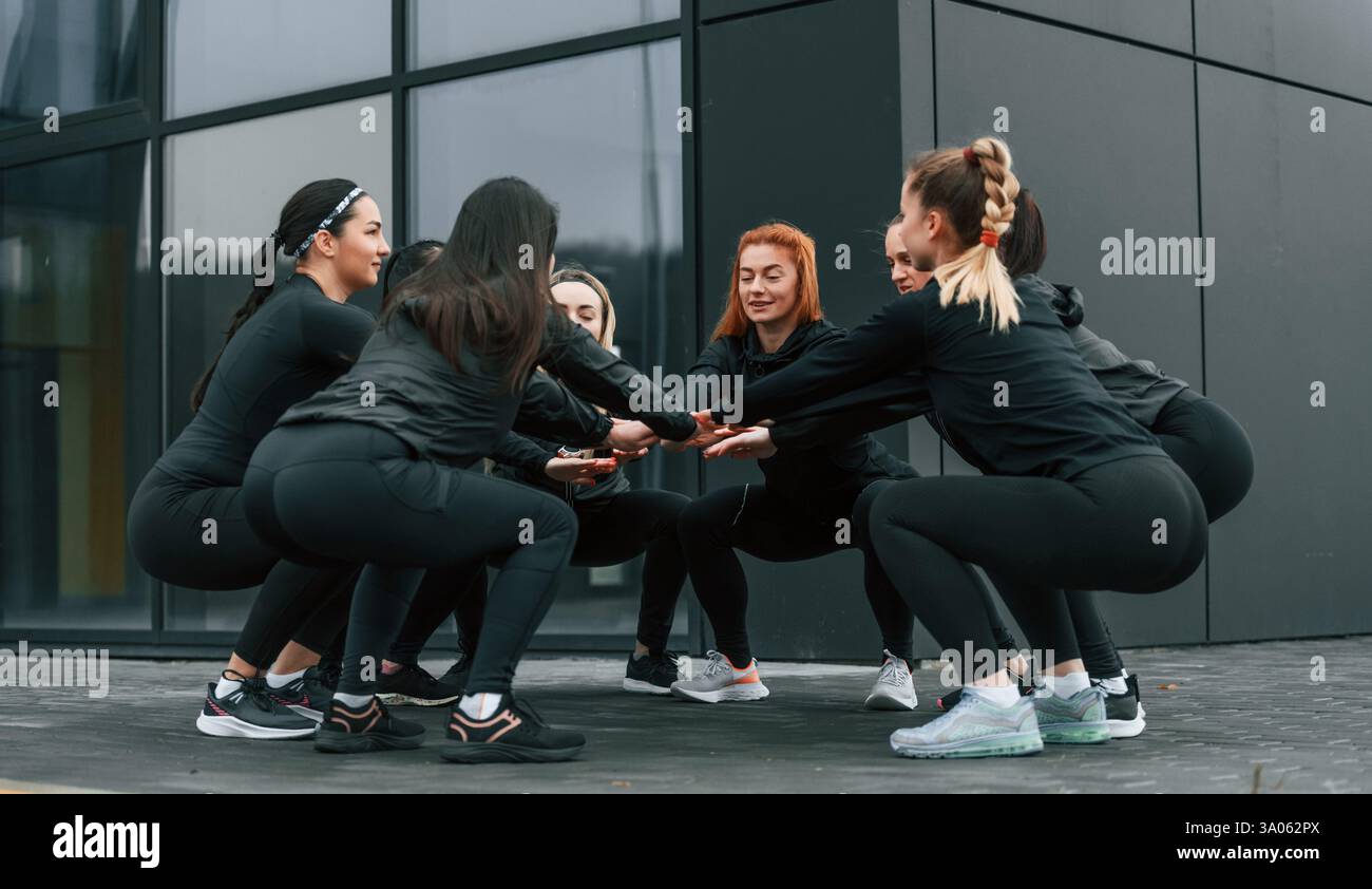 Concezione del lavoro di squadra. Un gruppo di donne sportive si trova all'aperto vicino all'edificio nero. Foto Stock