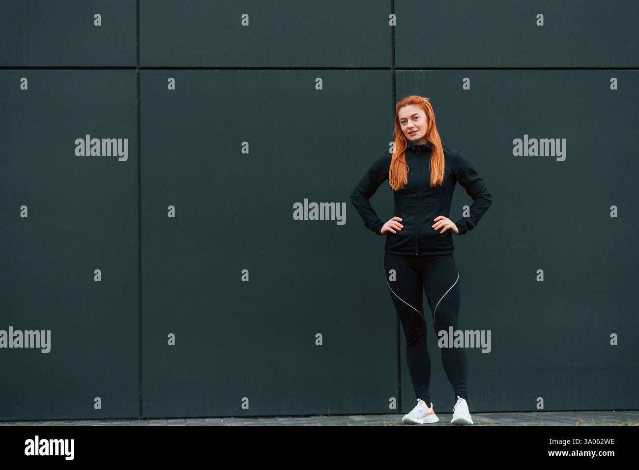 Le mani sono sulla vita. La donna è abbigliamento sportivo all'aperto contro l'edificio nero. Foto Stock