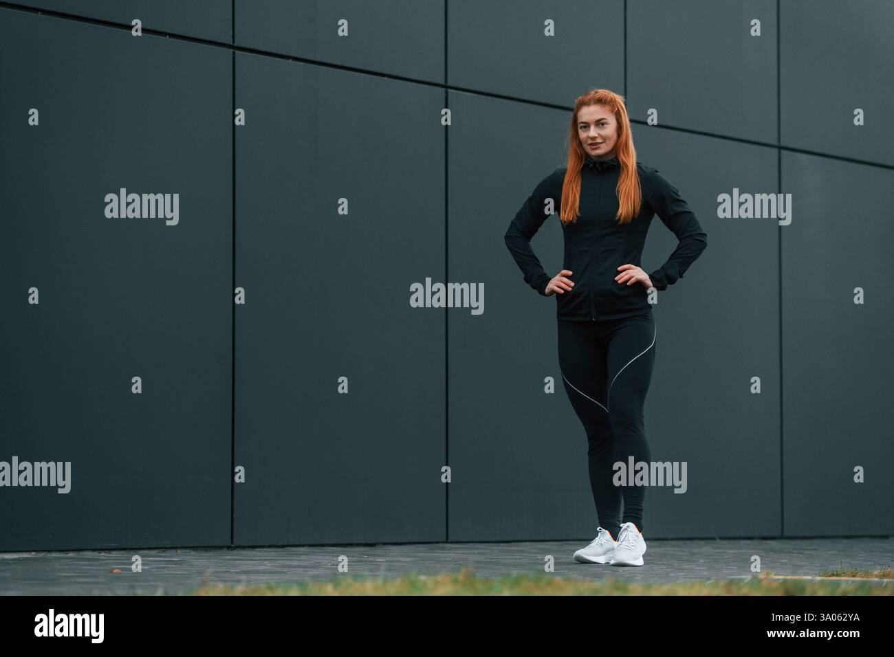 Le mani sono sulla vita. La donna è abbigliamento sportivo all'aperto contro l'edificio nero. Foto Stock