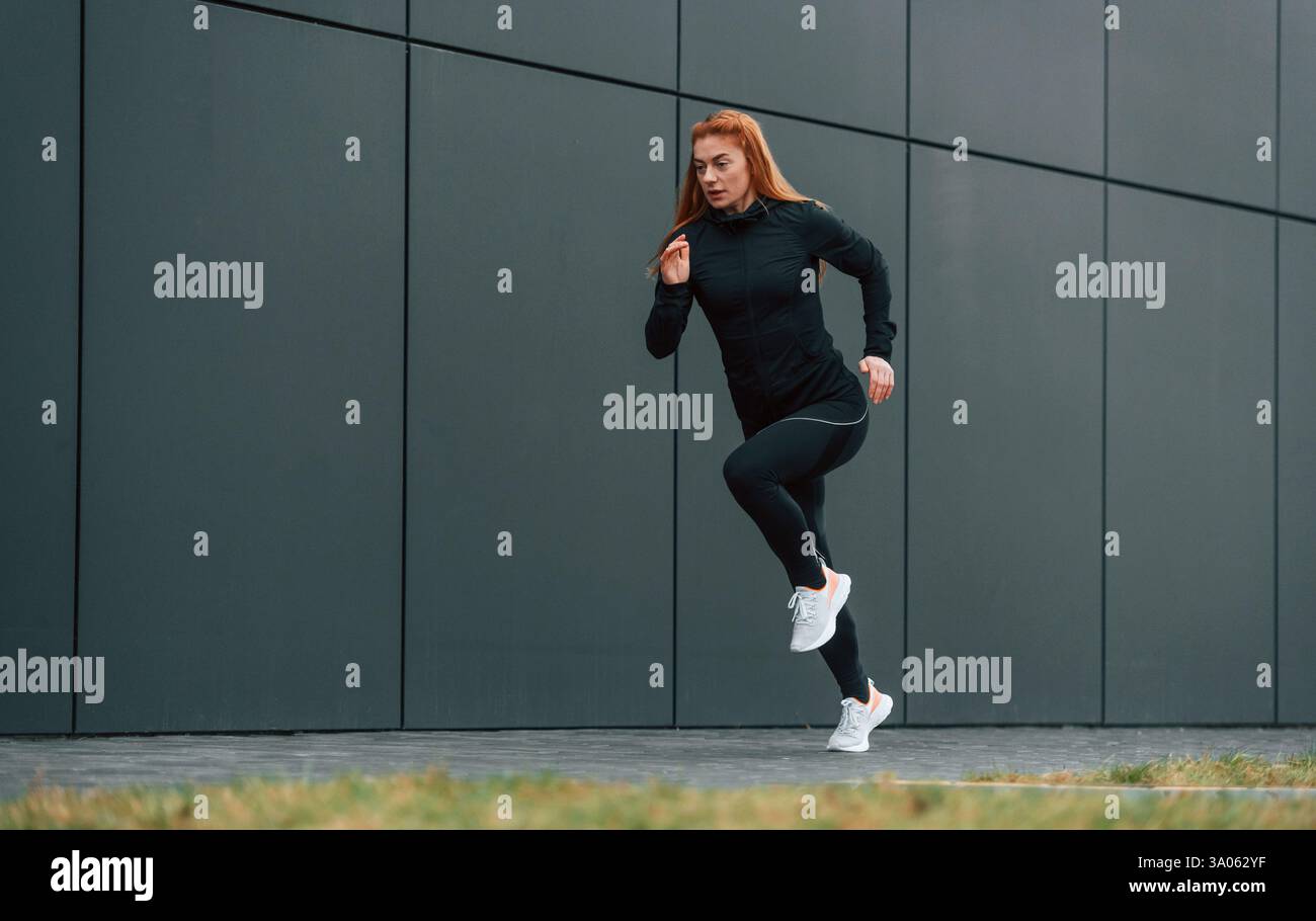 La donna è un abbigliamento sportivo che corre all'aperto contro un edificio nero. Foto Stock