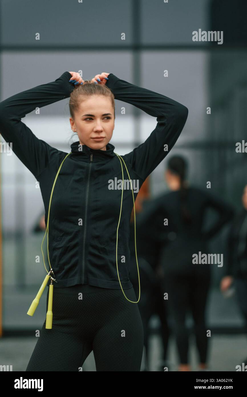 La bella donna è in piedi davanti ai suoi amici. Un gruppo di donne sportive si trova all'aperto vicino all'edificio nero. Foto Stock