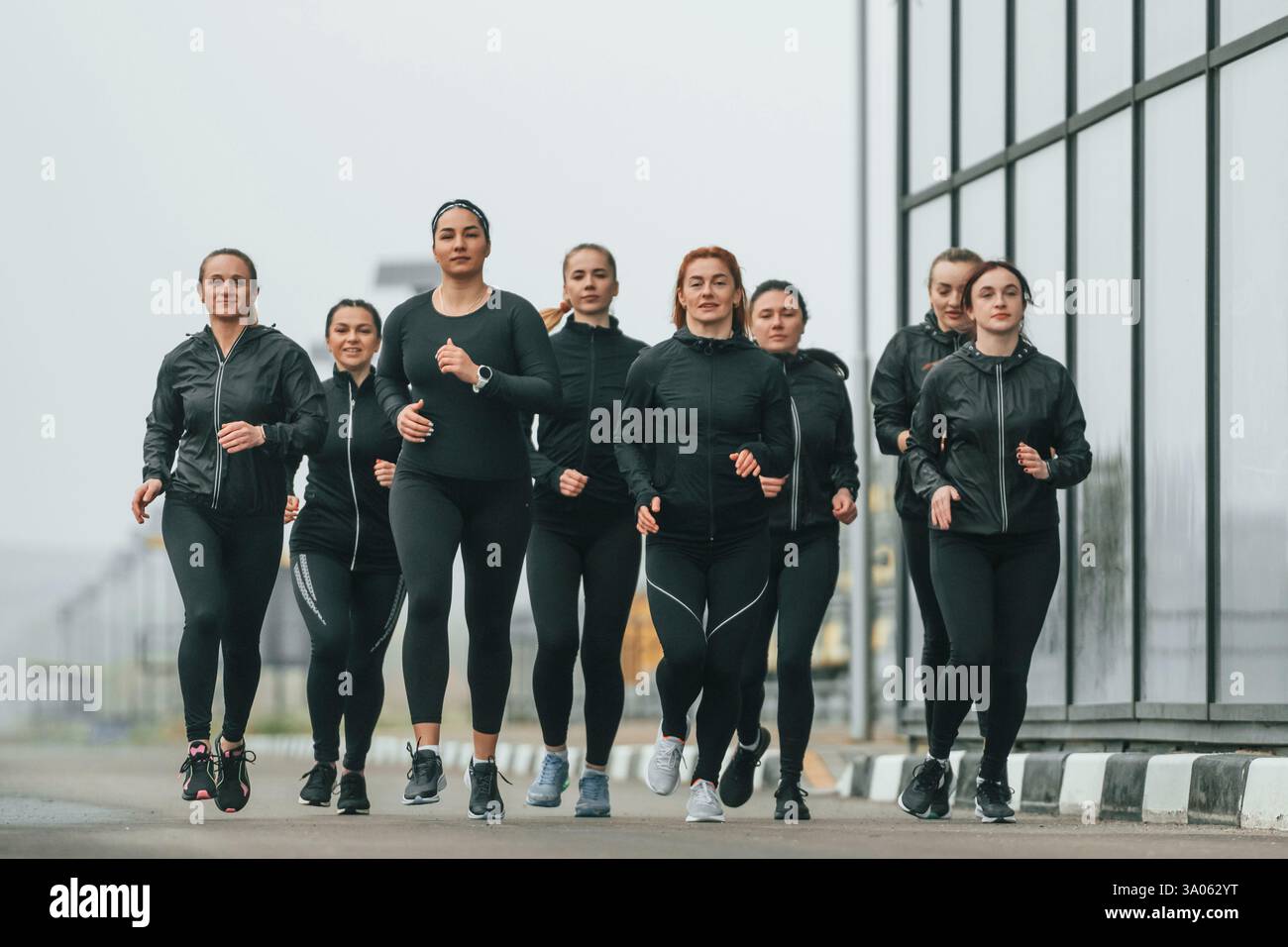Corsa mattutina. Un gruppo di donne sportive si trova all'aperto vicino all'edificio nero. Foto Stock