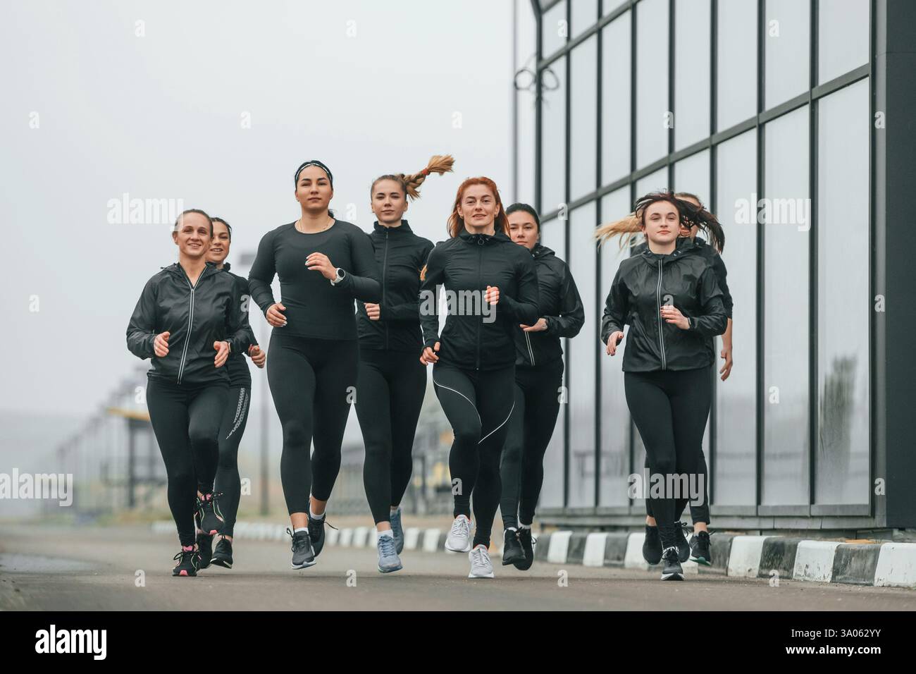 Corsa mattutina. Un gruppo di donne sportive si trova all'aperto vicino all'edificio nero. Foto Stock