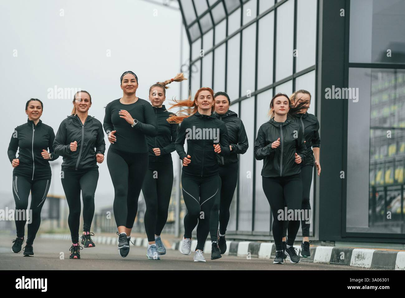 Corsa mattutina. Un gruppo di donne sportive si trova all'aperto vicino all'edificio nero. Foto Stock