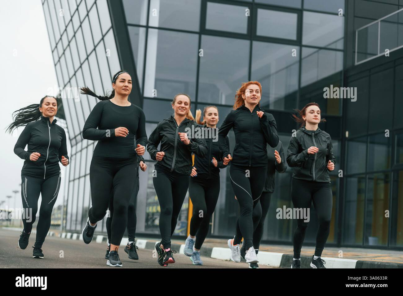 Corsa mattutina. Un gruppo di donne sportive si trova all'aperto vicino all'edificio nero. Foto Stock