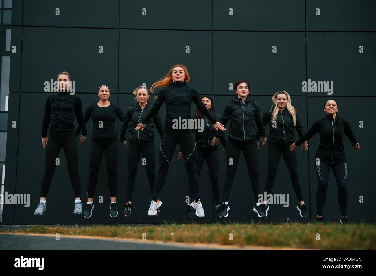 Saltando insieme. Un gruppo di donne sportive si trova all'aperto vicino all'edificio nero. Foto Stock