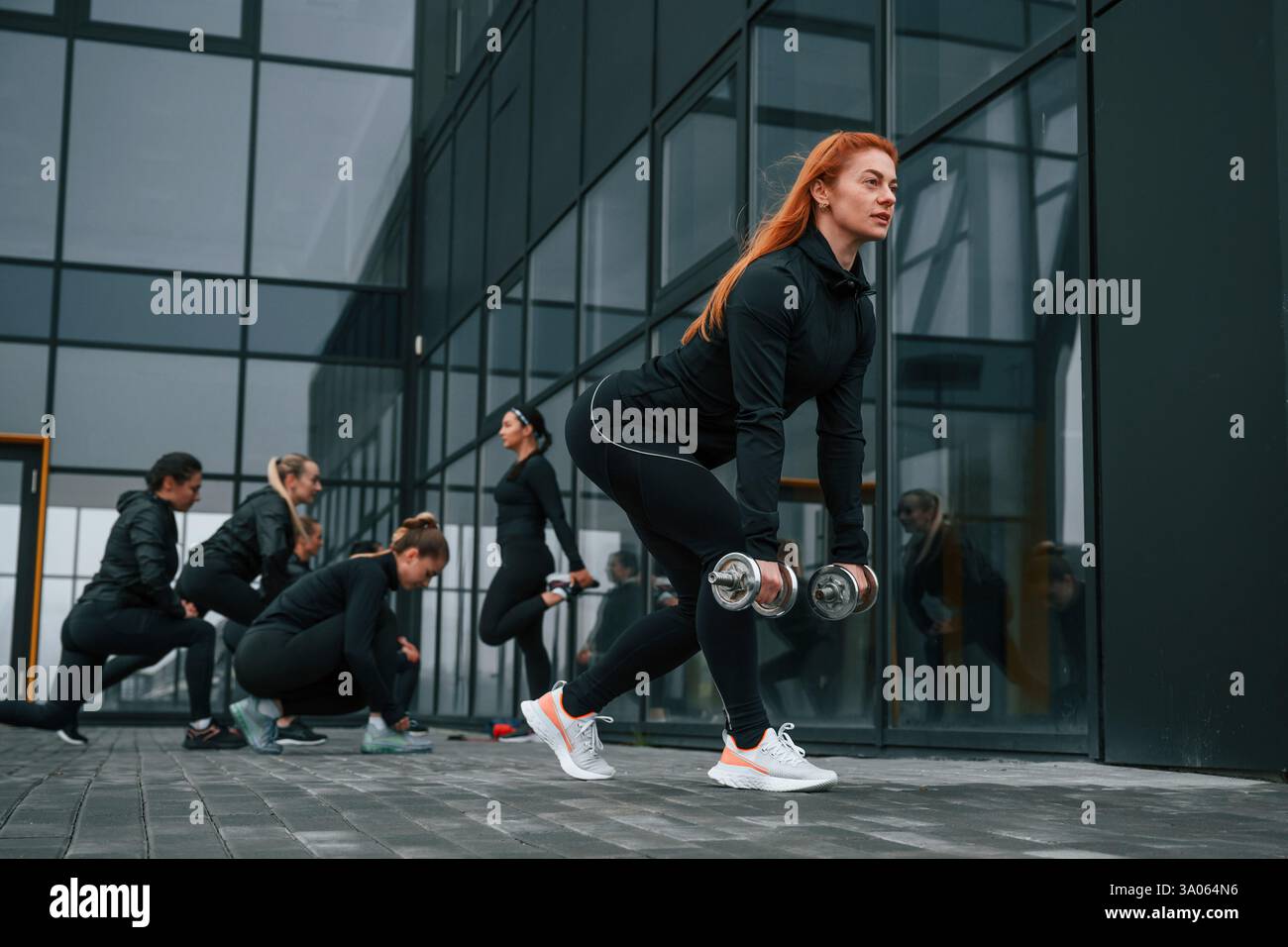 Sollevamento manubri. Un gruppo di donne sportive si trova all'aperto vicino all'edificio nero. Foto Stock