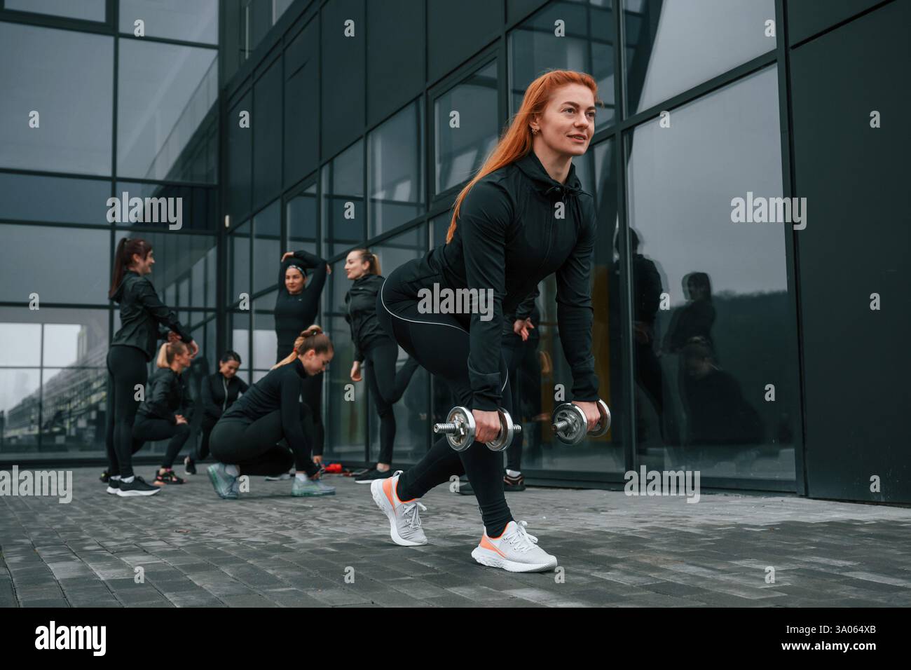 Sollevamento manubri. Un gruppo di donne sportive si trova all'aperto vicino all'edificio nero. Foto Stock