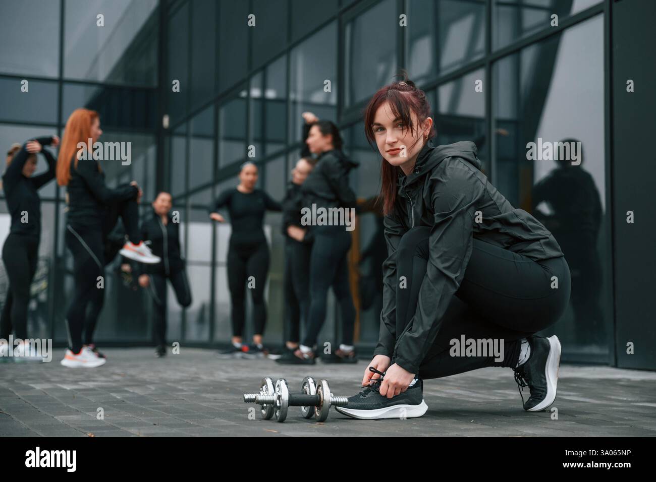 Lacci di lacci. Un gruppo di donne sportive si trova all'aperto vicino all'edificio nero. Foto Stock