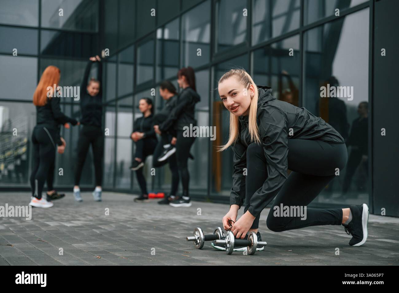 Lacci di lacci. Un gruppo di donne sportive si trova all'aperto vicino all'edificio nero. Foto Stock