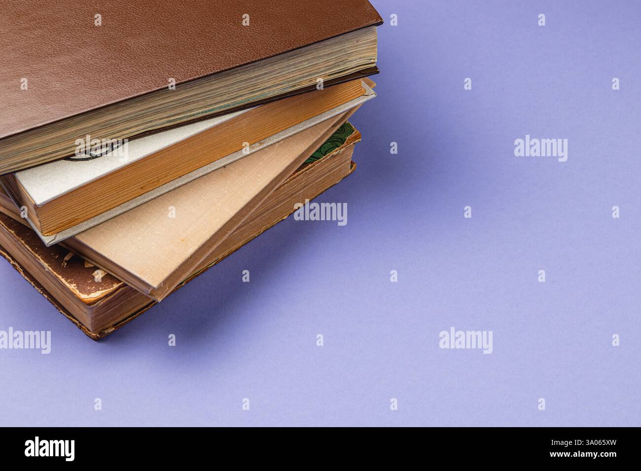 Una raccolta di libri è impilata l'una sull'altra su un morbido sfondo viola. I diversi design e colori della copertina aggiungono un tocco visivo al Foto Stock