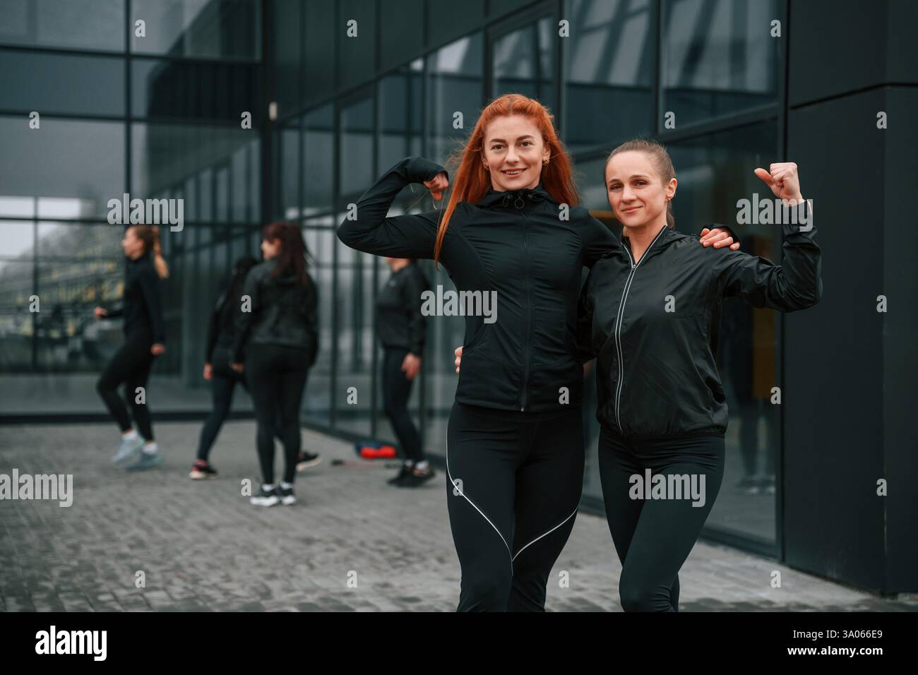 In piedi con le braccia in alto, mostrando muscoli, concezione del lavoro di squadra. Un gruppo di donne sportive è all'aperto. Foto Stock
