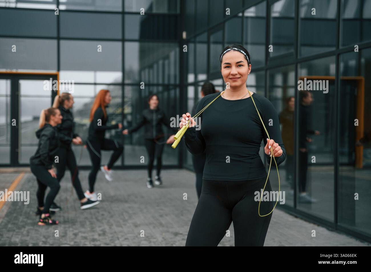 Con corda gialla. Un gruppo di donne sportive si trova all'aperto vicino all'edificio nero. Foto Stock