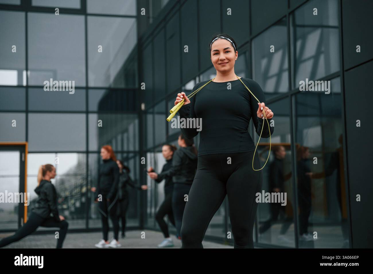 Con corda gialla. Un gruppo di donne sportive si trova all'aperto vicino all'edificio nero. Foto Stock