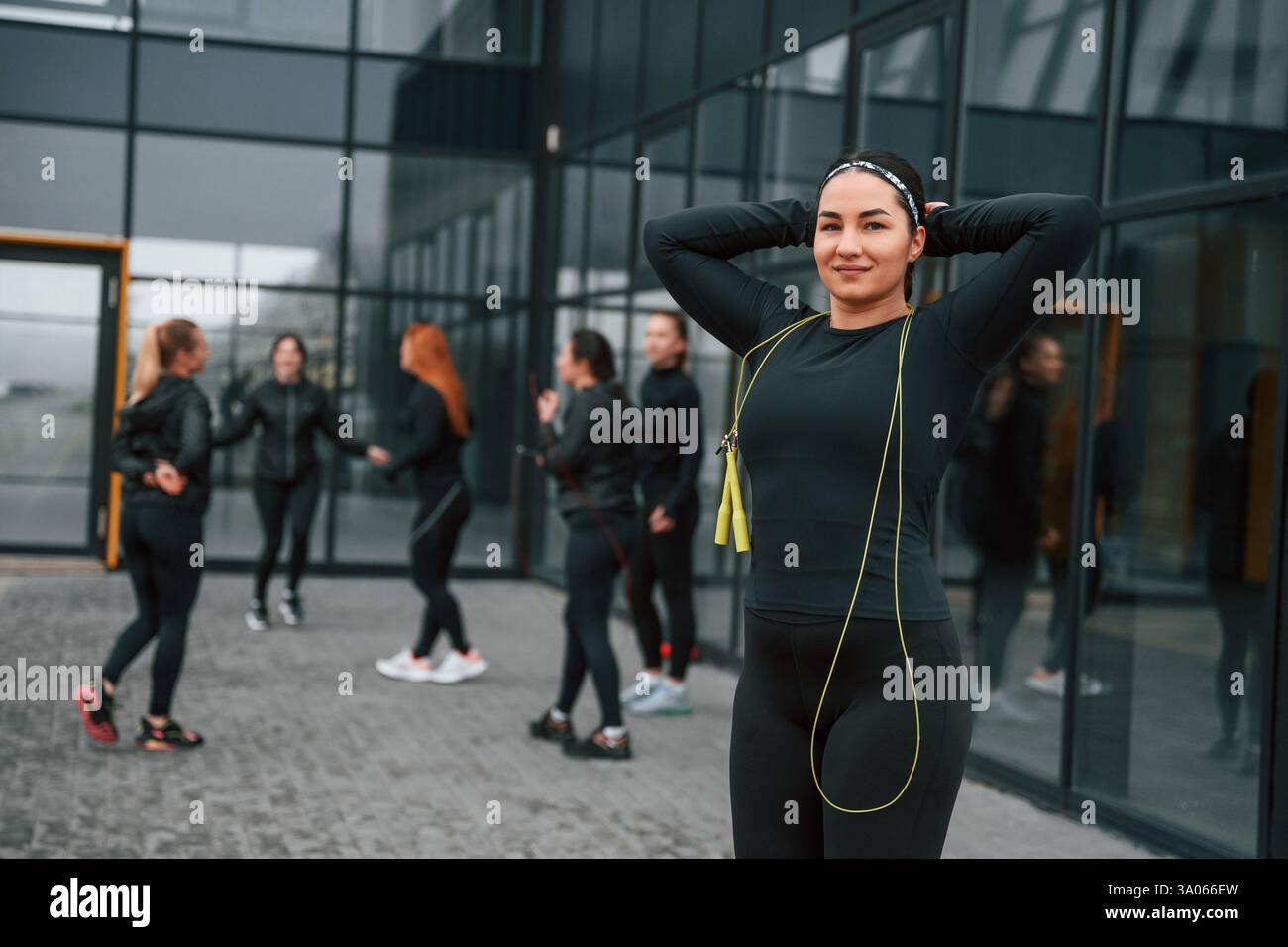 Con corda gialla. Un gruppo di donne sportive si trova all'aperto vicino all'edificio nero. Foto Stock