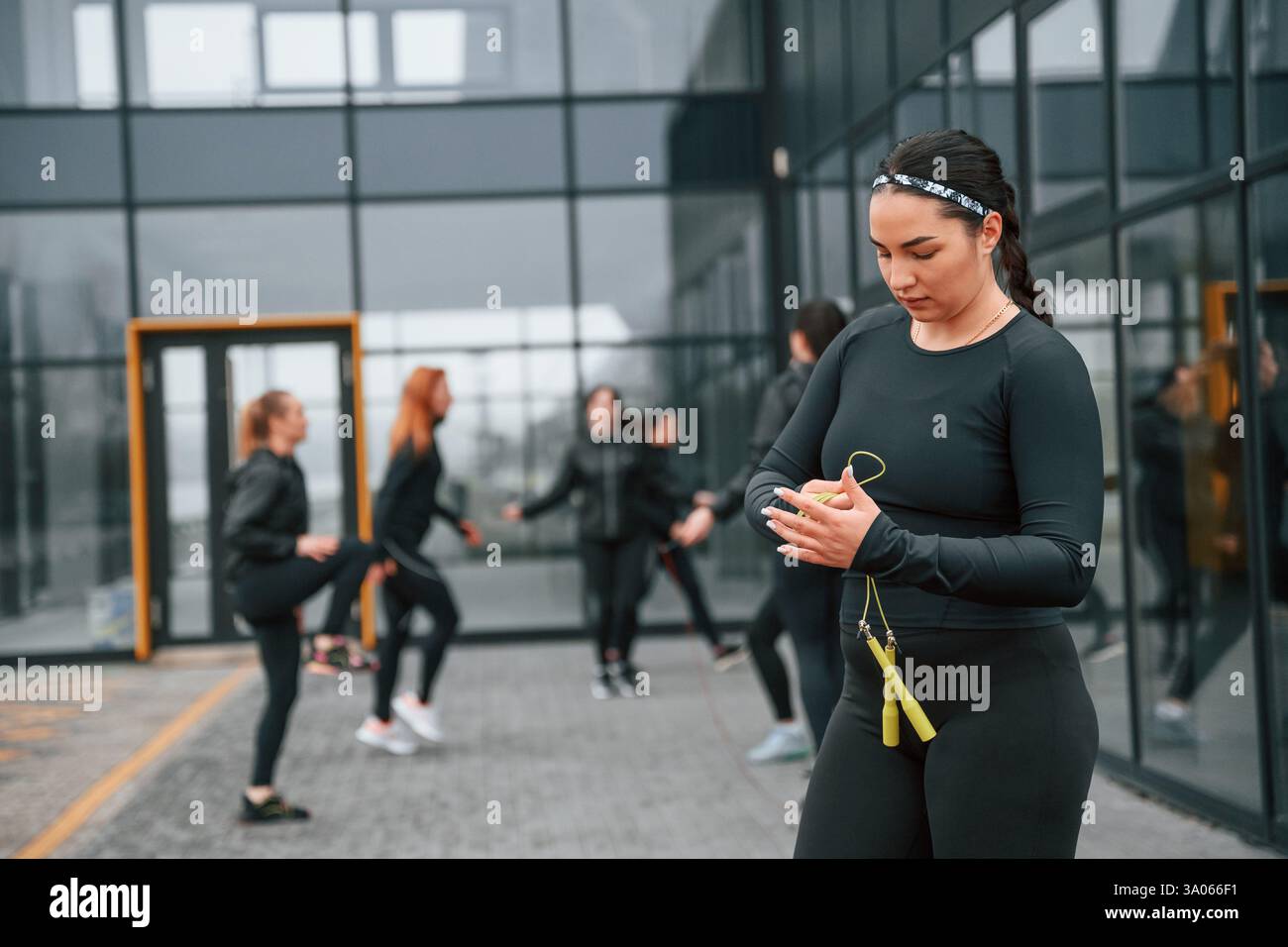 Con corda gialla. Un gruppo di donne sportive si trova all'aperto vicino all'edificio nero. Foto Stock