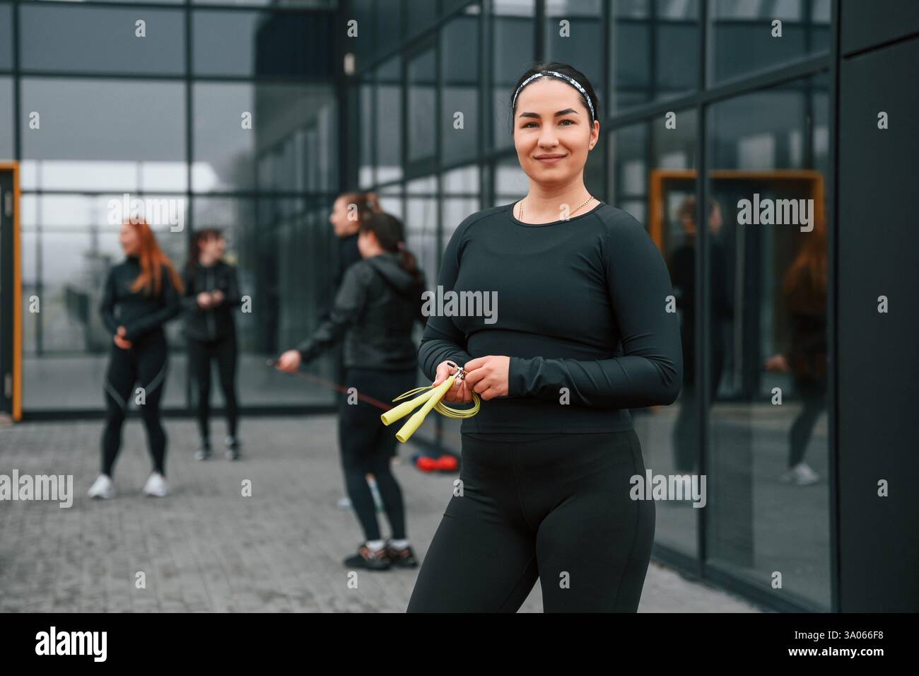 Con corda gialla. Un gruppo di donne sportive si trova all'aperto vicino all'edificio nero. Foto Stock