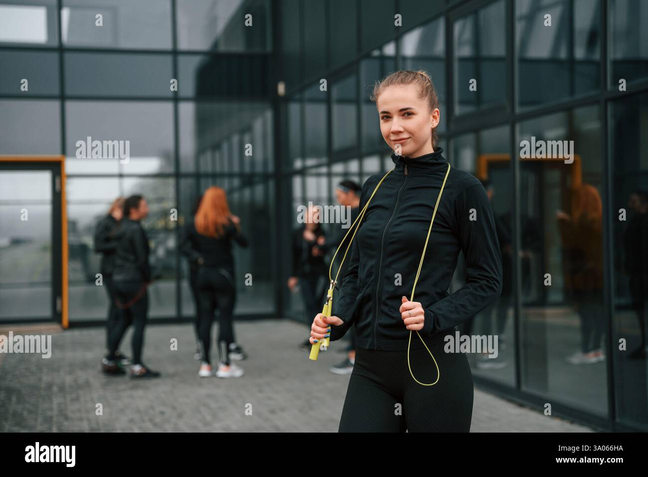 In piedi con la corda per saltare. Un gruppo di donne sportive si trova all'aperto vicino all'edificio nero. Foto Stock