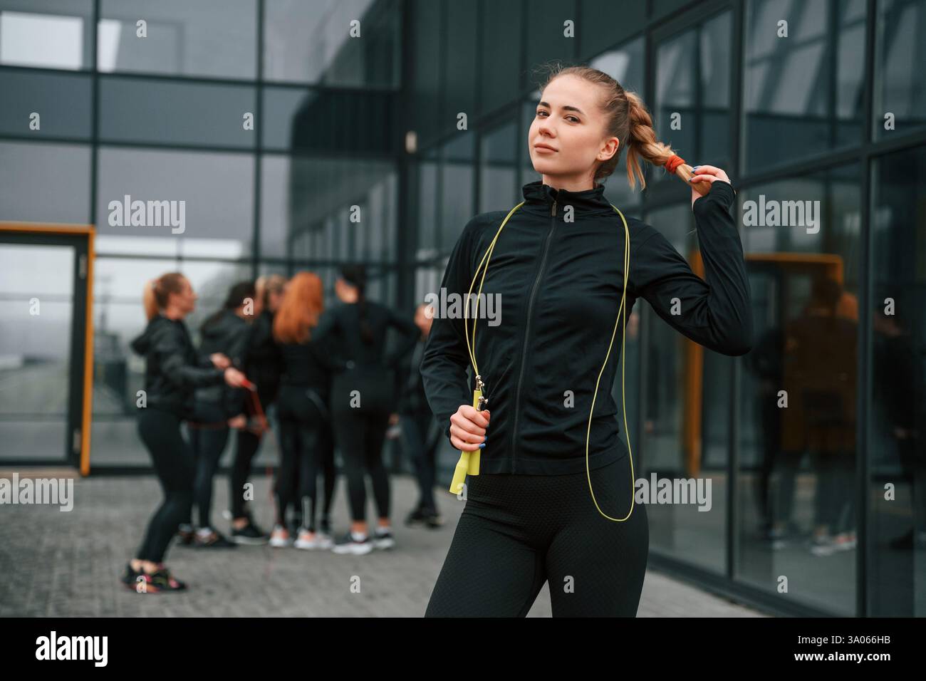 In piedi con la corda per saltare. Un gruppo di donne sportive si trova all'aperto vicino all'edificio nero. Foto Stock