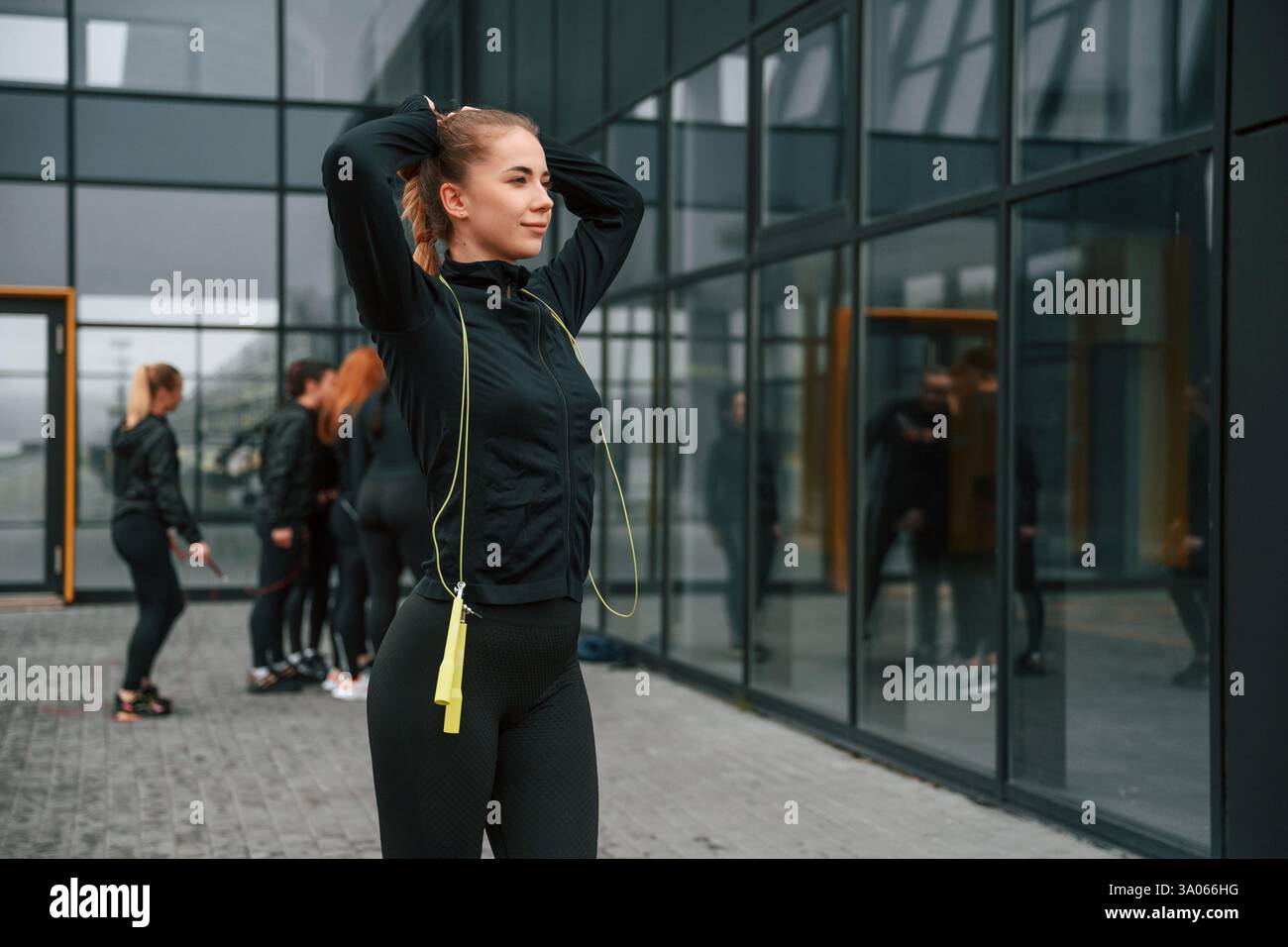 In piedi con la corda per saltare. Un gruppo di donne sportive si trova all'aperto vicino all'edificio nero. Foto Stock