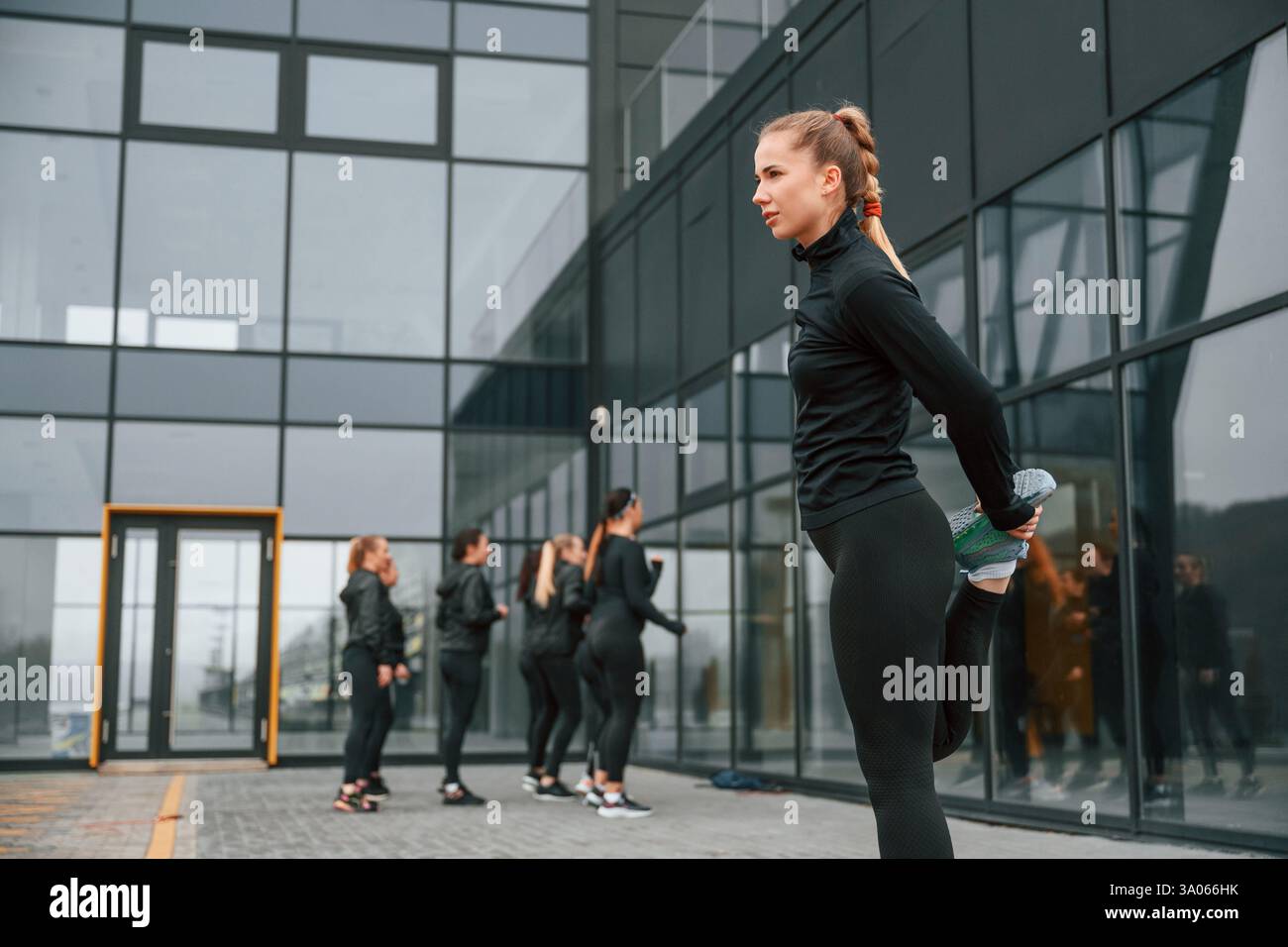 Esercizi di riscaldamento. Un gruppo di donne sportive si trova all'aperto vicino all'edificio nero. Foto Stock