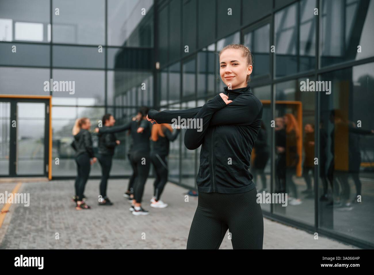 Esercizi di riscaldamento. Un gruppo di donne sportive si trova all'aperto vicino all'edificio nero. Foto Stock