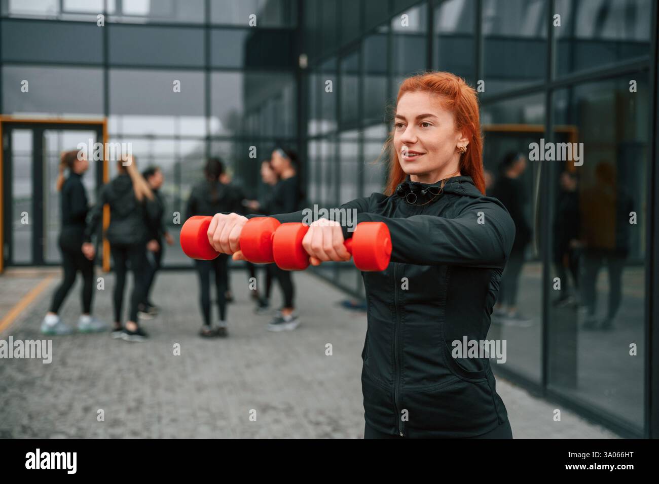Tenendo i manubri. Un gruppo di donne sportive si trova all'aperto vicino all'edificio nero. Foto Stock
