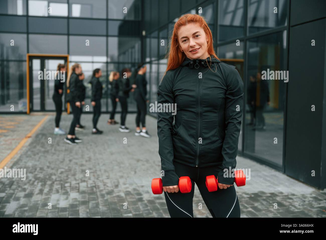 Tenendo i manubri. Un gruppo di donne sportive si trova all'aperto vicino all'edificio nero. Foto Stock