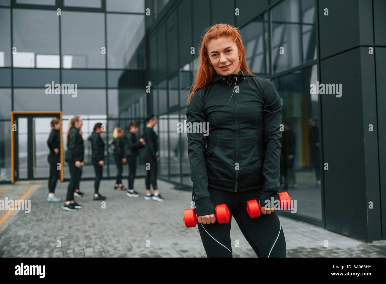 Tenendo i manubri. Un gruppo di donne sportive si trova all'aperto vicino all'edificio nero. Foto Stock